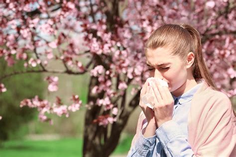 Sneezing young girl with nose wiper among blooming trees in park ...