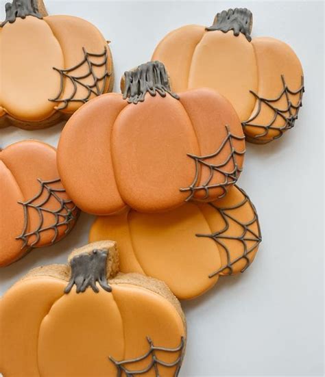 pumpkin cookies decorated with icing and spider webs on white table top next to each other