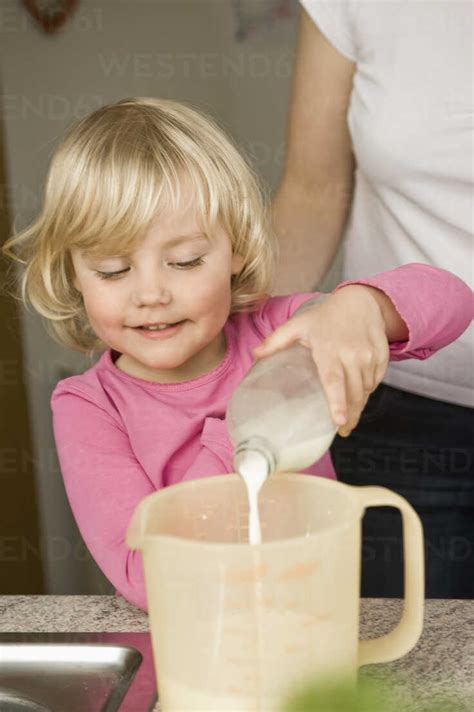 Mother and daughter pouring milk into measuring cup stock photo