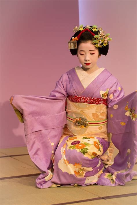 a geisha doll sitting on the ground in front of a purple wall