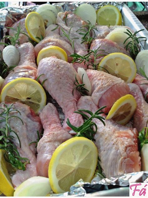 raw chicken with lemons, rosemary and garlic on the side in a baking pan