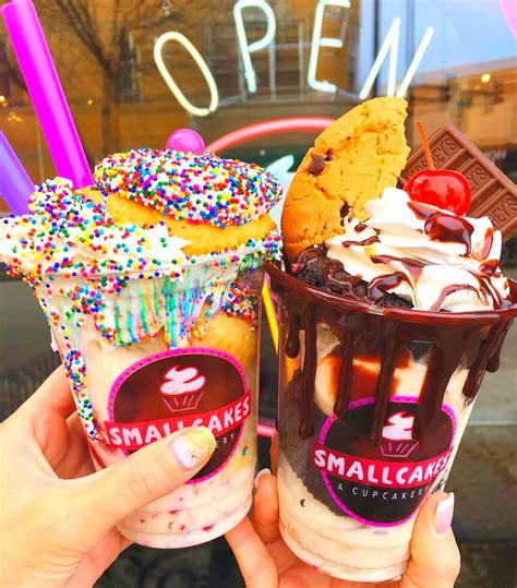 two ice cream sundaes with sprinkles and cookies are being held up in front of a store window