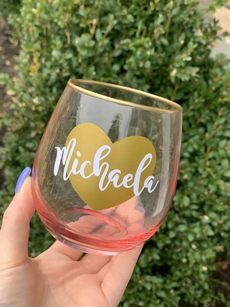 a person holding up a wine glass with the word michael on it in front of some bushes
