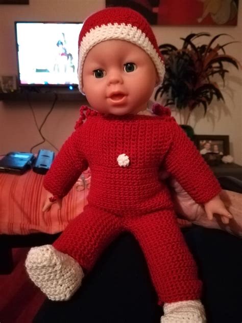 the doll is wearing a red knitted outfit and white booties, while sitting in front of a flat ...