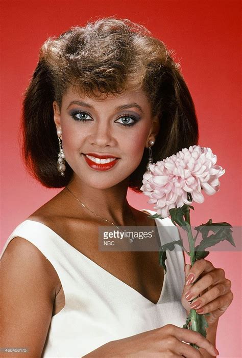 a woman holding a pink flower in her right hand and smiling at the camera while wearing a white ...