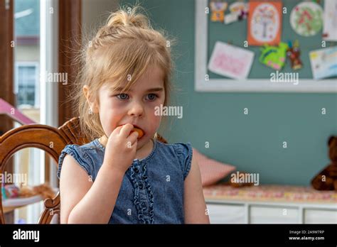 Very cute young girl, with pretty blue eyes, sitting at the kitchen table eating an orange Stock ...