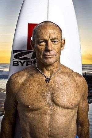 a man with no shirt standing in front of a surfboard on the beach at sunset