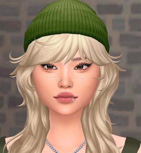 a woman with blonde hair wearing a green beanie and diamond necklace, standing in front of a ...