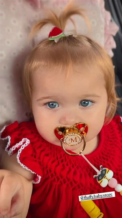 a baby girl wearing a red dress with a clock on it's face and a pacifier in her mouth