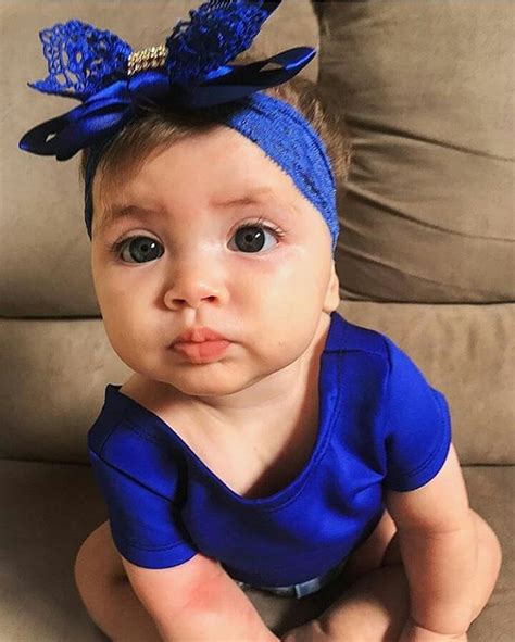 a baby wearing a blue shirt with a bow on it's head sitting on a couch