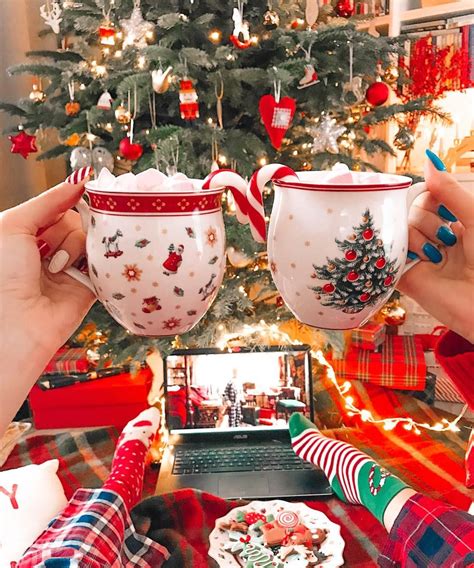 two people holding up mugs in front of a christmas tree with presents on it