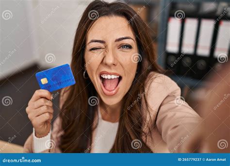 Young Brunette Woman Working at Small Business Ecommerce Holding Credit Card Winking Looking at ...
