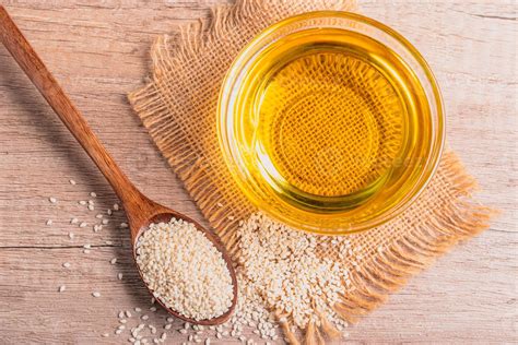 sesame oil in a bowl and white sesame seeds on wooden background ...