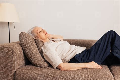 Aged woman sleeping on a couch. Senior female lying on a sofa in living room with closed eyes ...