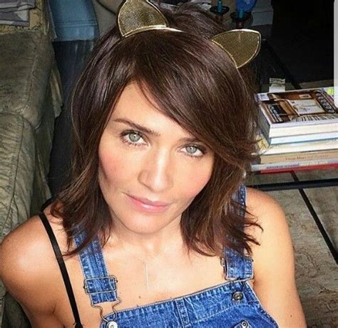 a woman in overalls with cat ears on her head sitting on a couch looking at the camera