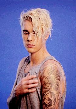 a man with blonde hair and tattoos on his arms is standing in front of a blue background