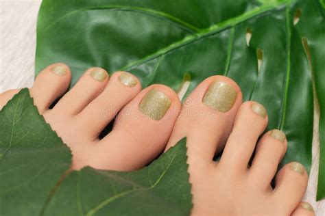 Female Feet with Yellow Glitter Nail Design. Gold Nail Polish Pedicure and Greel Leaves on ...