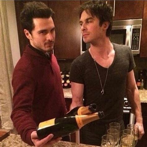 two men standing in a kitchen holding wine bottles and glasses