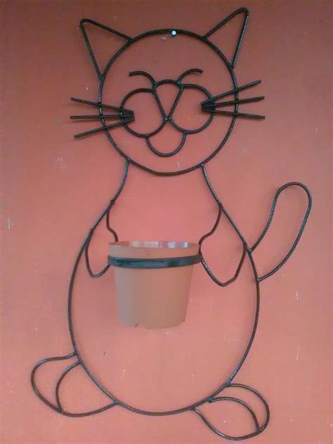 a metal cat with a cup on it's back hanging from the side of a wall