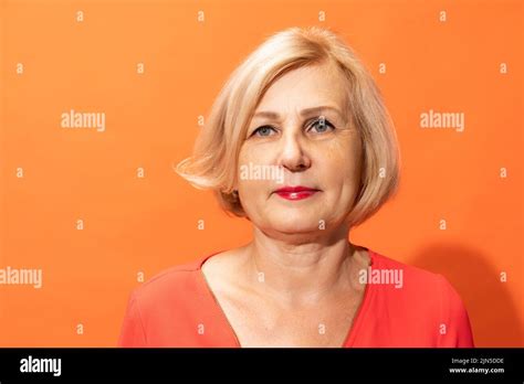 Half-length portrait of beautiful middle age woman with blond hair posing isolated on orange ...