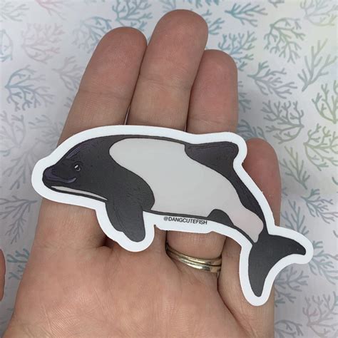 a hand holding a black and white dolphin sticker