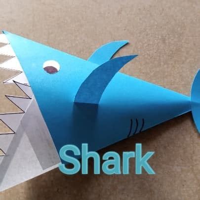 an origami shark made out of paper on a table with the word shark cut out