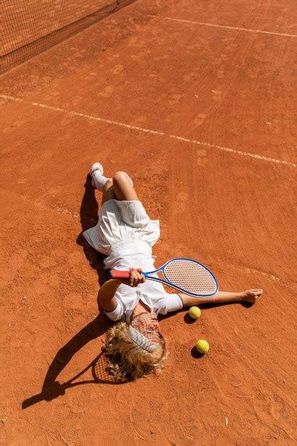 Una joven se acuesta en la cancha de tenis de césped con un traje deportivo blanco | Foto Premium