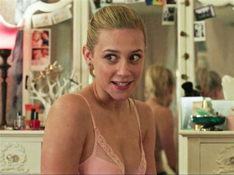 a woman wearing a bra smiling at the camera in front of a dresser and mirror