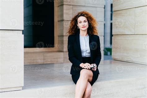 Attractive young woman wearing black formal suit, sitting crossed legs