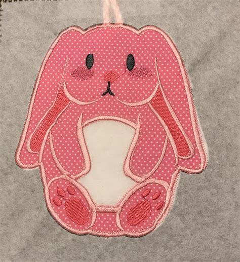 a pink bunny rabbit applique hanging on a gray wall with white polka dots