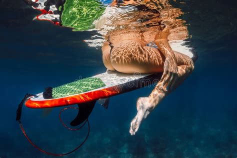 Attractive Surf Girl Sitting on Surfboard in Blue Ocean. Underwater