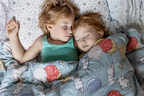 Two little sibling girls sisters sleeping in an embrace in bed under