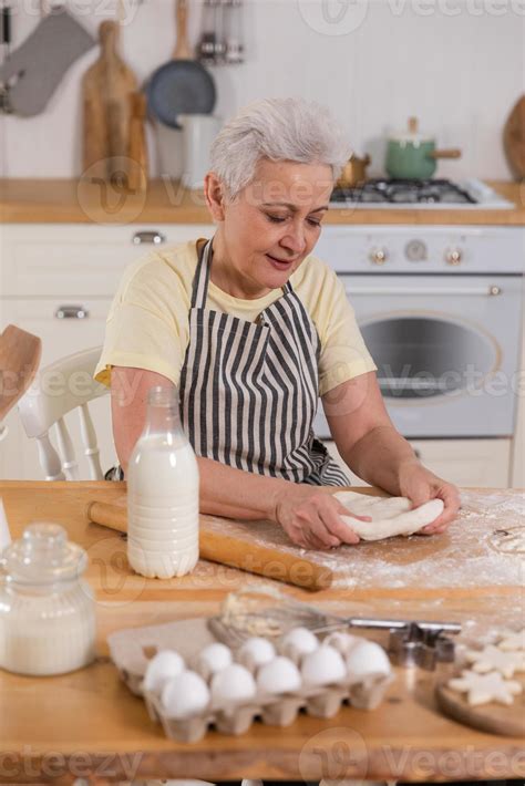 Happy senior woman cooking in kitchen. Stylish older mature gray haired