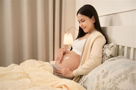 Beautiful pregnant woman applying moisturizing, stretch mark cream on