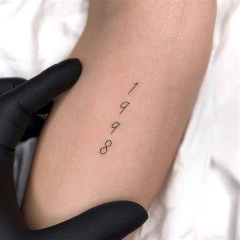 "1998" lettering tattoo placed on the inner forearm.