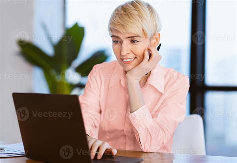 Smiling Mature Woman At Laptop Browsing Internet Working At Workplace In Modern Office. Computer