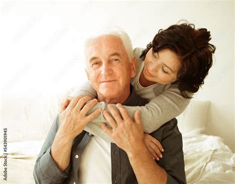 Mature 60 year old couple hugging while sitting on the bed in the