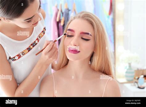 Professional artist creating makeup for beautiful model in room Stock ...