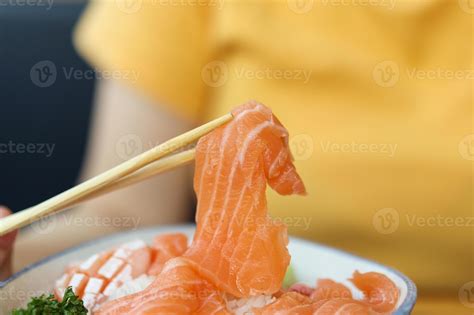Asian woman eating salmon slice sashimi with rice in Japanese
