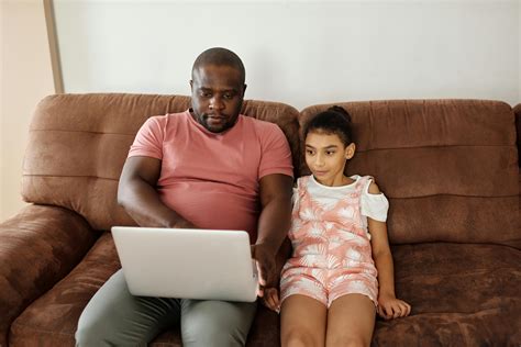 Father and Daughter Sitting on a Sofa and Looking at a Laptop · Free