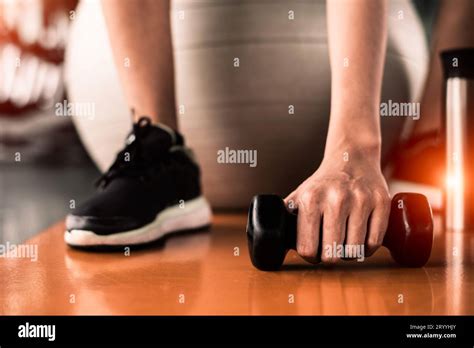 Close up of sport woman sitting on yoga ball and grab dumbbell on floor by hand in fitness sport