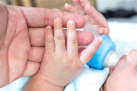 The baby's left hand is holding his father's hand while drinking milk ...