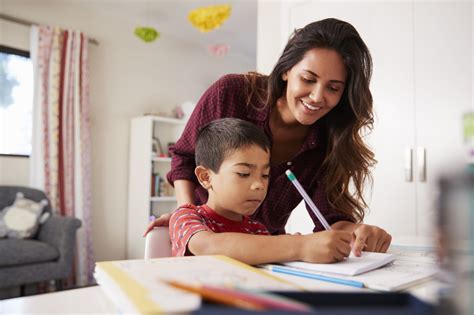Mother Helping Son With Homework Sitting At Desk In Bedroom - MAEC