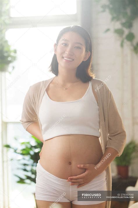 Felice giovane incinta asiatico donna toccare pancia e sorridente a