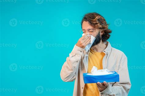 Man blowing out nose with napkin isolated on blue. Winter cold concept
