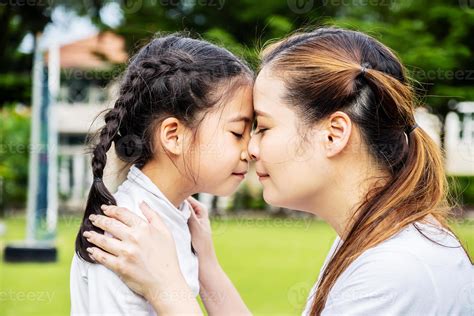 Cute asian mother and little daughter hugging and kissing in park
