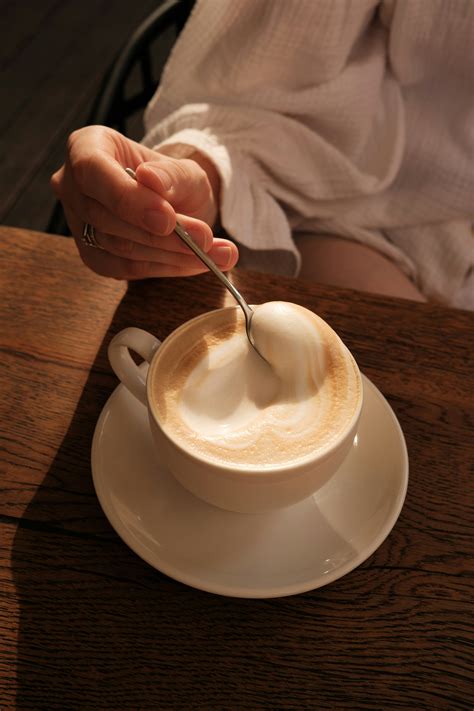 A person holding a spoon in a cup of coffee photo – Free Coffee Image