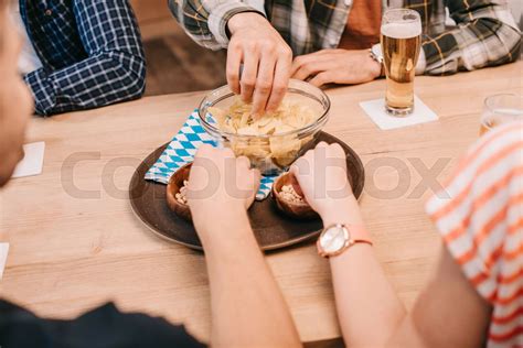 partial view of friends taking snacks from bowls while sitting together ...