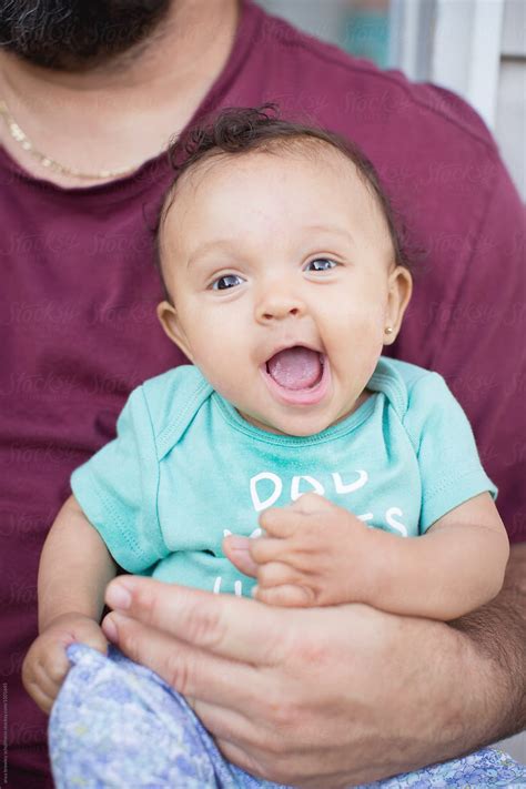 "A Baby Smiling Happily As She Is Held By Her Father" by Stocksy