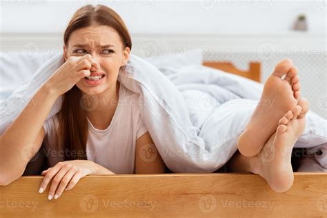 Stinky Feet. Disgusted Girlfriend Pinching Nose Lying Near Boyfriend's